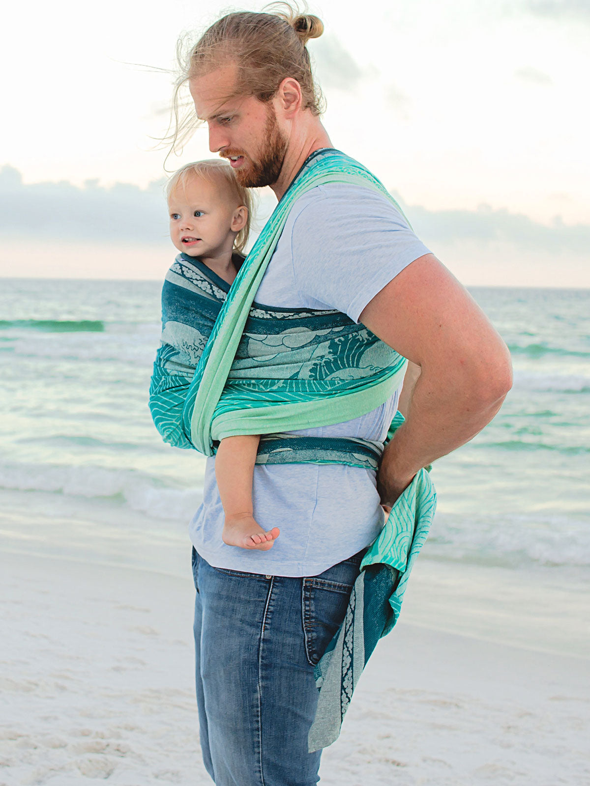 Man carrying a child in a sling on a beach