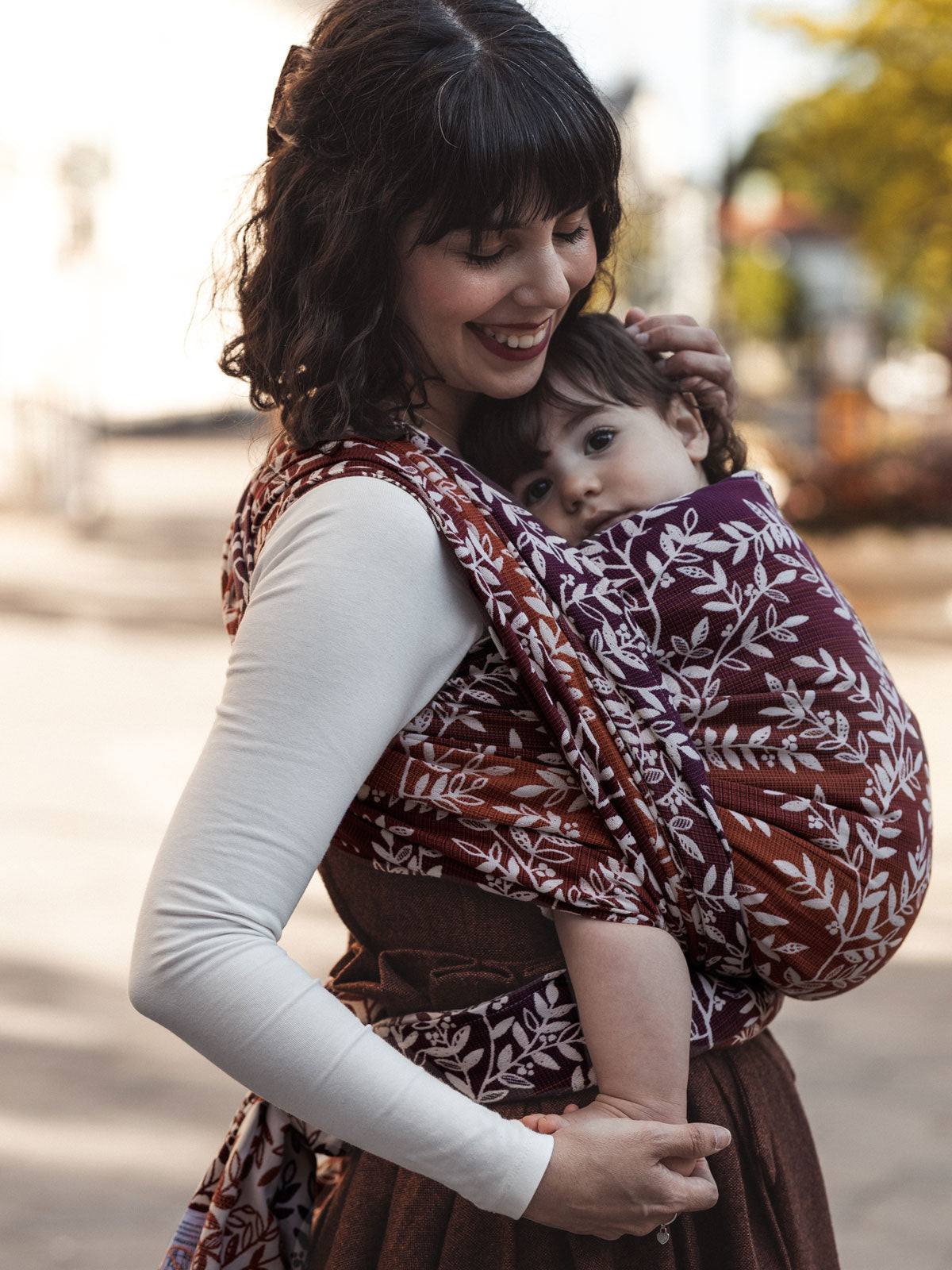 Woman carrying a child in a patterned baby sling outdoors