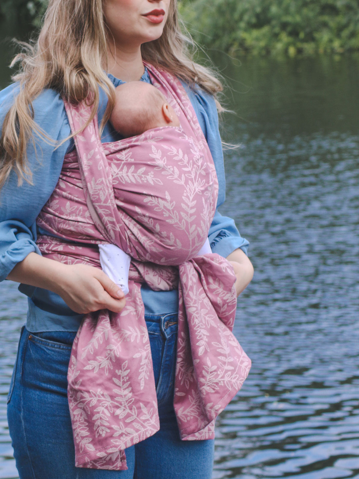 Woman holding a baby in a pink sling by a body of water