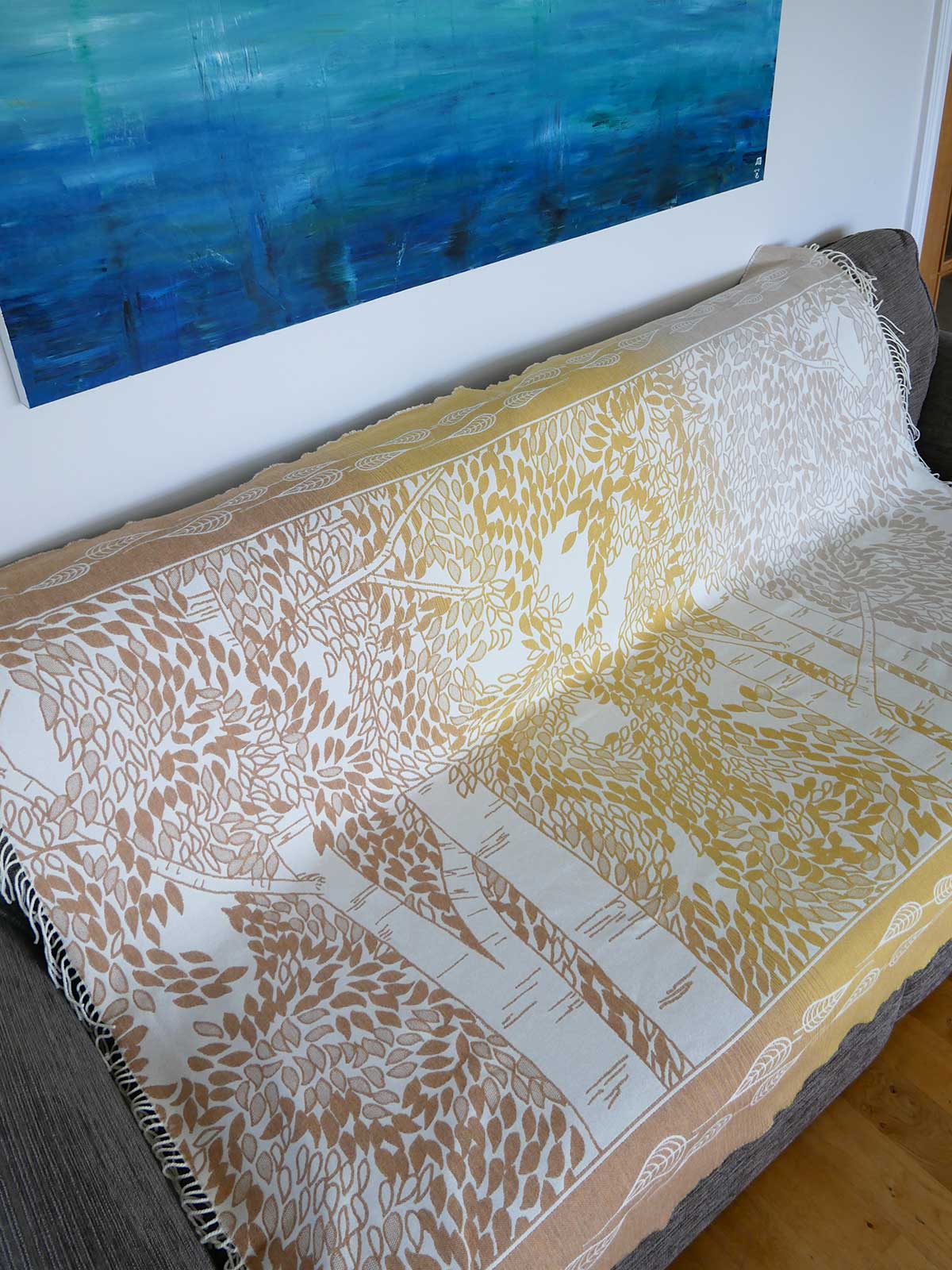 Patterned Dryad Rustling Grove Merino Throw draped over a surface with a painting in the background