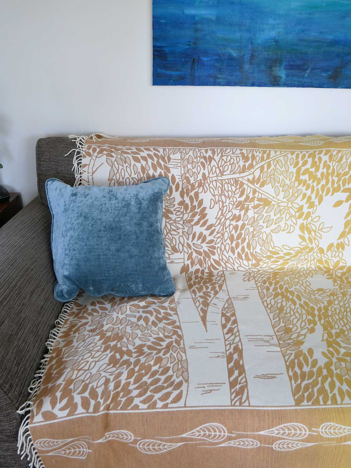 Blue pillow on a patterned blanket with a painting in the background