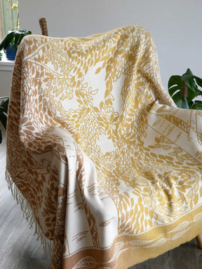 Yellow and white patterned blanket draped over a chair with plants in the background
