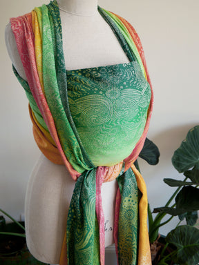 Mannequin wearing a colourful Marina Starburst Baby Wrap with a green patterned top against a white background