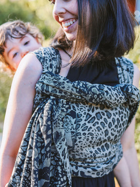 Woman wearing a leopard print Prowl Savannah Baby Wrap with a child in the background