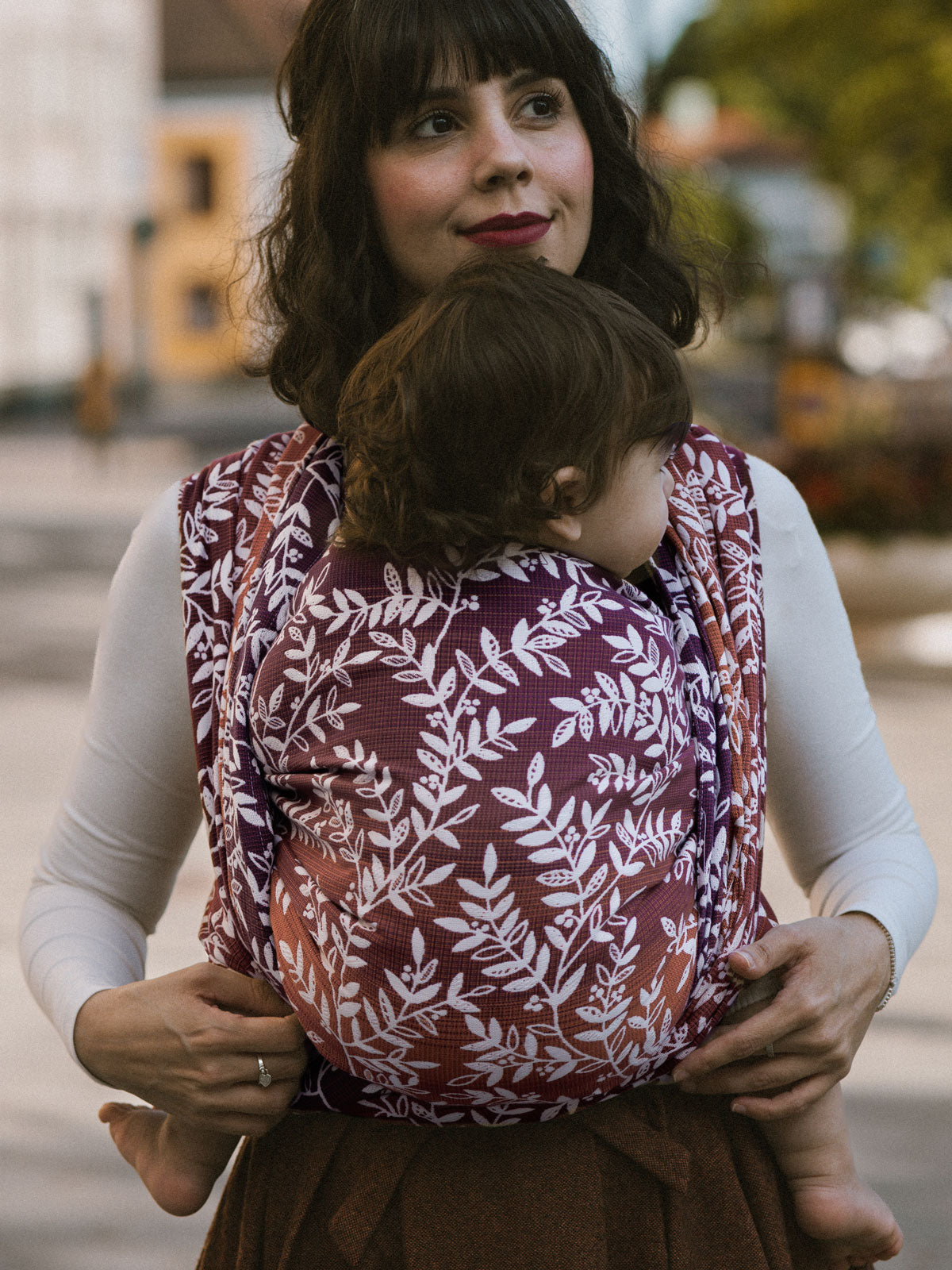 Woman carrying a child in a Willow Herbstlaub Baby Wrap outdoors.