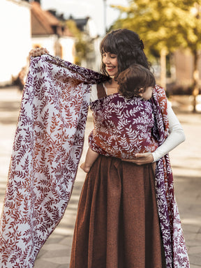 Woman holding a baby in a sling with a floral patterned wrap outdoors.